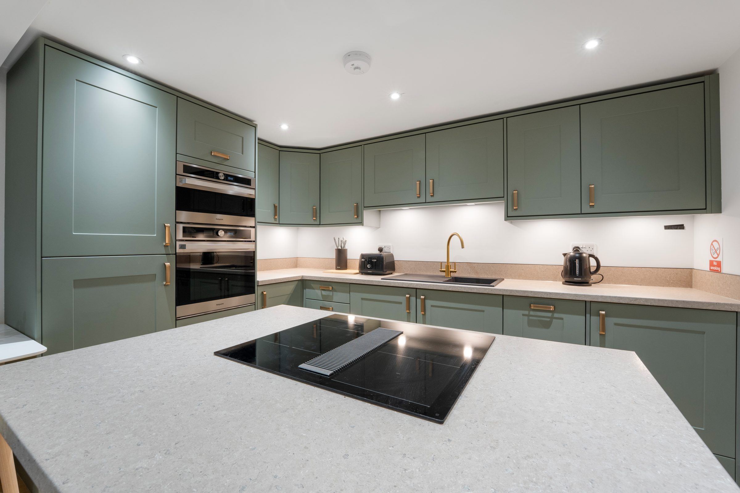 Green kitchen with a white island and induction hob