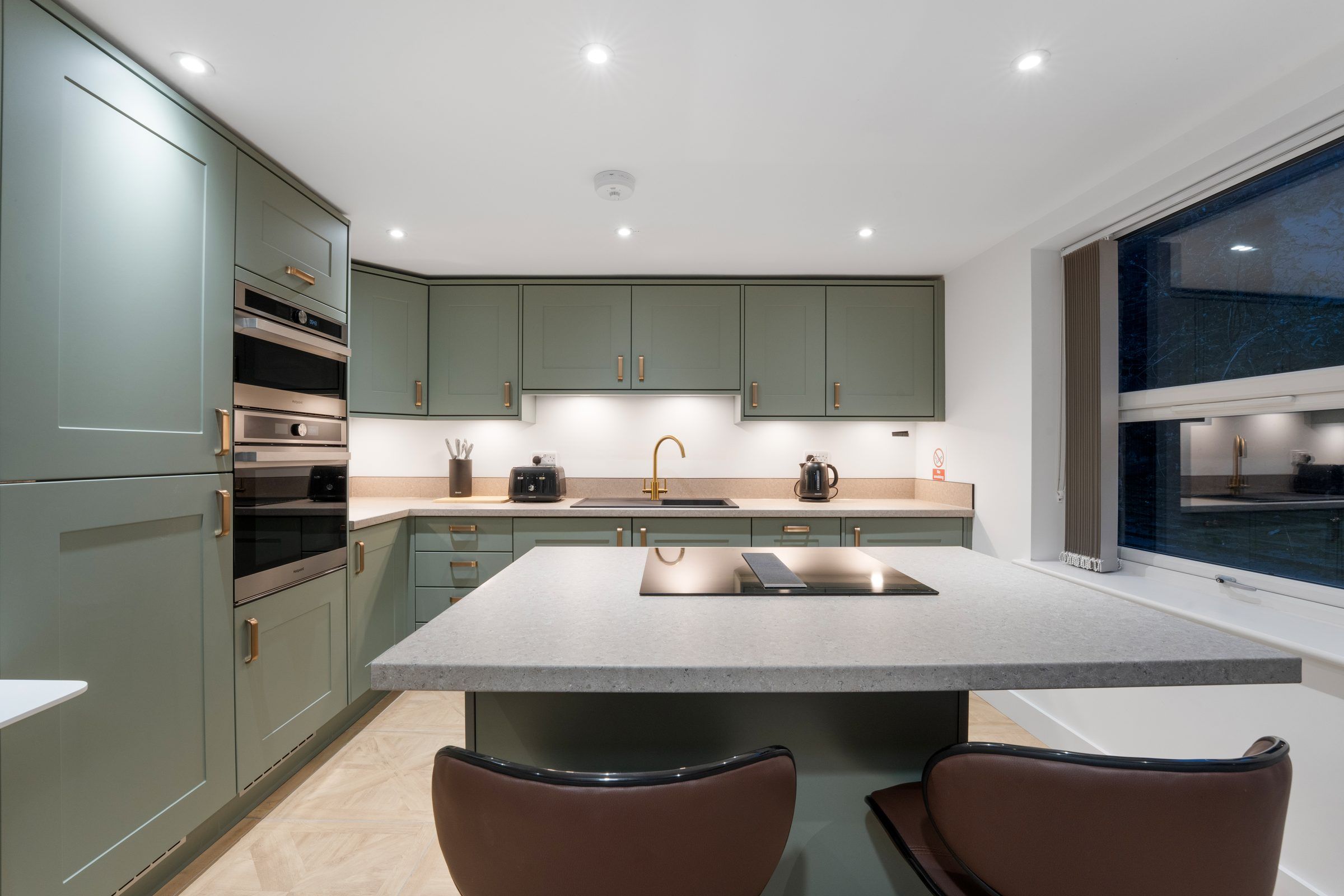 Kitchen with green cabinets, island and bar stools
