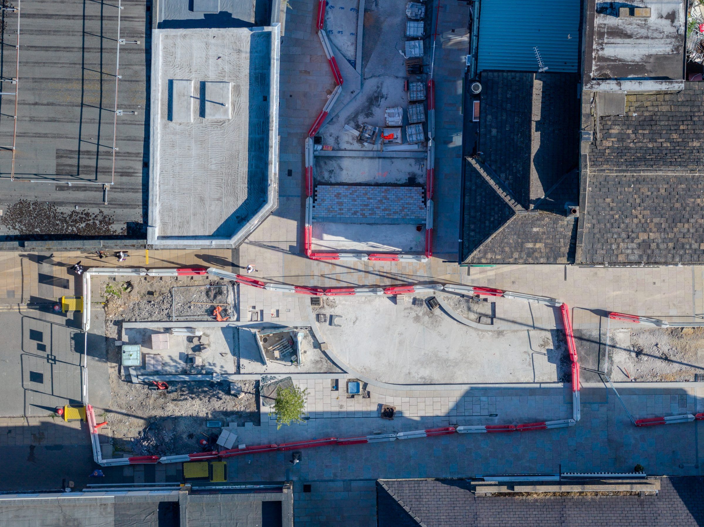 Top-down view of a cleared plot fenced off beside a shopping street