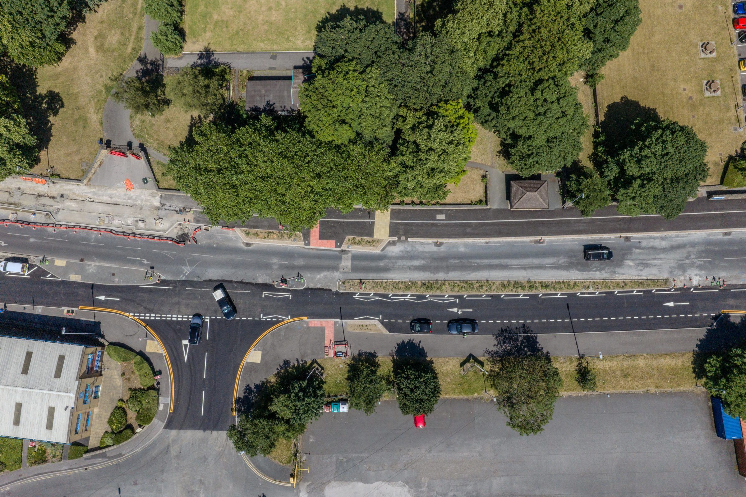 Top-down view of a dual carriageway beside trees and industrial units